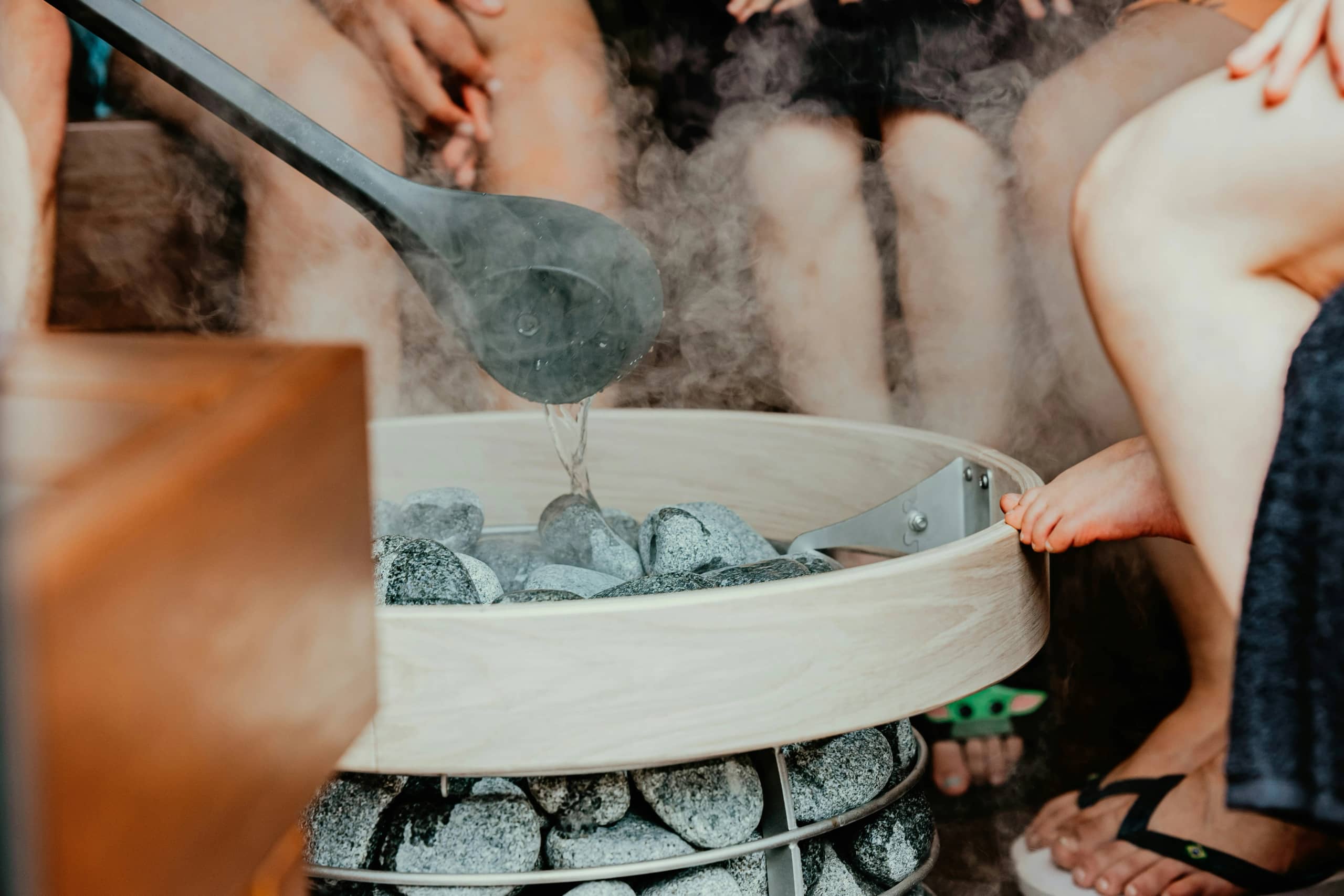 Person adding water to hot sauna rocks creating steam